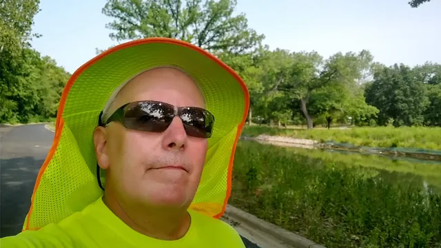 John today in a hi-vis shirt, sun hat, and sunglasses beside a park pond